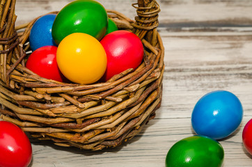 Decorated Easter eggs in wicker basket on rustic background. Easter basket filled with colorful eggs on a wooden background 