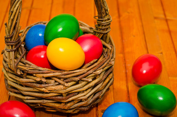 Decorated Easter eggs in wicker basket on rustic background. Easter basket filled with colorful eggs on a wooden background 