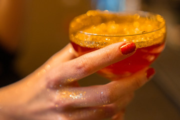 Golden cocktail glass at the bar. Young women's hand holding a martini glass with a golden stardust...