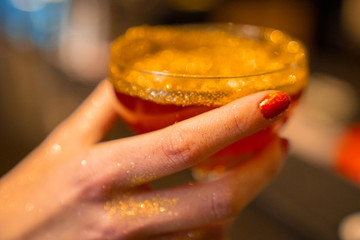 Golden cocktail glass at the bar. Young women's hand holding a martini glass with a golden stardust...