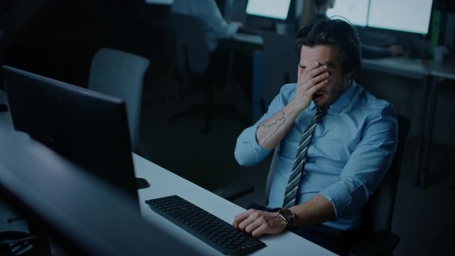In the Office at Night Overworked Tired Office Worker Uses Desktop Computer Yawns. Tired Exhausted Businessman Finishing Important Project