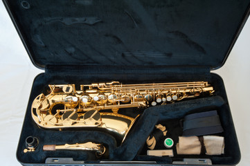 A gold / brass alto saxophone on white background with pearl keys - laid out in case with accessories