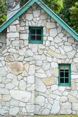 Small wooden windows and chimney stack in a stone cottage with green trim and gable