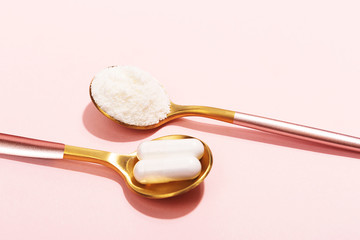 Collagen powder and pills on pink background. Extra protein intake. Natural beauty and health supplement for skin, bones, joints and gut. Plant or fish based. Flat lay, top view. Copy space.