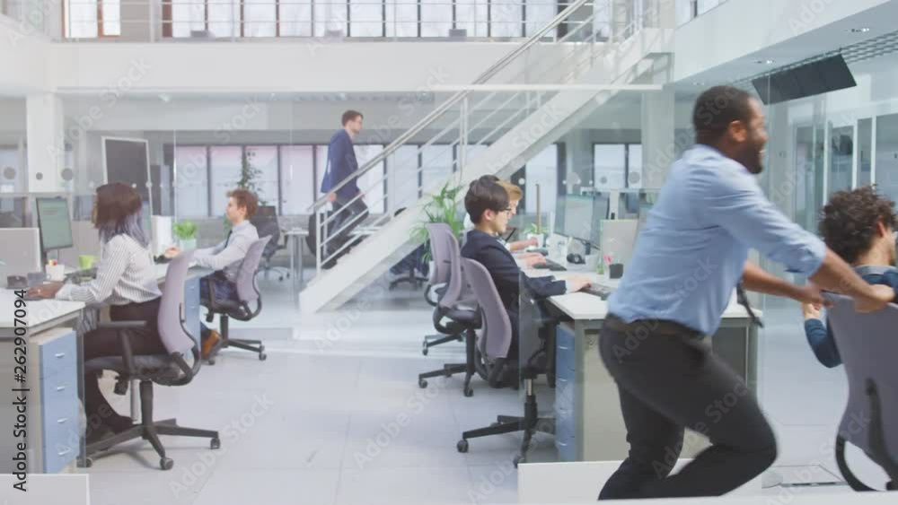 Aufkleber cheerful employee pushes his handsome colleague on a chair next to rows of desks with diverse busine