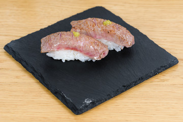 nigiri of heat-burned kobe beef dressed with mustard, served on a square plate of slate