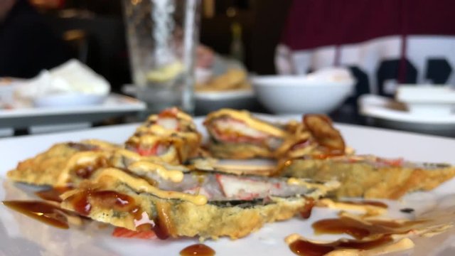 First-person POV shot: eating tasty fried sushi rolls at a restaurant, picking food with chopsticks.