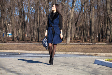 Portrait of a young beautiful woman in blue coat with a bag walking in spring park