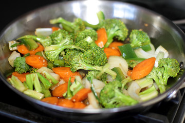 Stir fried vegetables cooking in a stainless steel pan.
