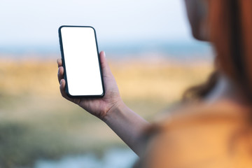 Mockup image of woman's hand holding black mobile phone with blank desktop screen by the beach and sea