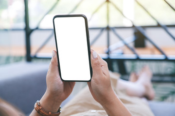 Mockup image of a woman holding black mobile phone with blank white desktop screen while laying down in living room with feeling relaxed