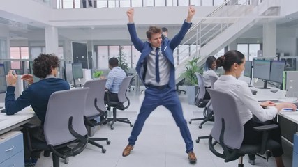 Young Cheerful Handsome Business Manager Wearing a Suit and Tie Dances in the Office. Diverse and Motivated Business People Work on Computers in Modern Open Office. - Powered by Adobe