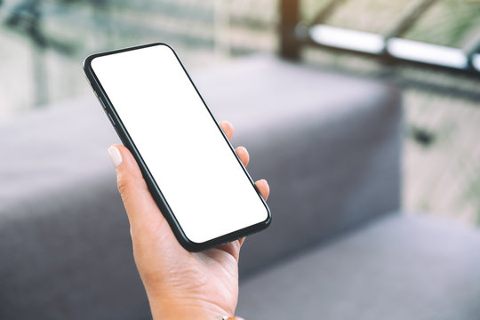 Mockup Image Of A Woman's Hand Holding Black Mobile Phone With Blank White Desktop Screen While Sitting In Living Room With Feeling Relaxed