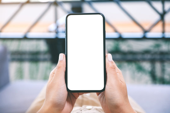 Mockup image of a woman holding black mobile phone with blank white desktop screen while laying down in living room with feeling relaxed