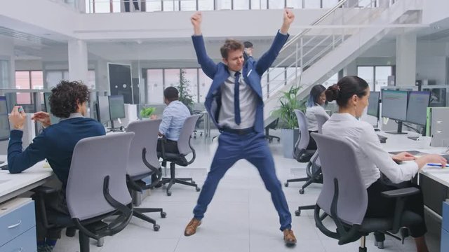 Young Cheerful Handsome Business Manager Wearing a Suit and Tie Dances in the Office. Diverse and Motivated Business People Work on Computers in Modern Open Office.