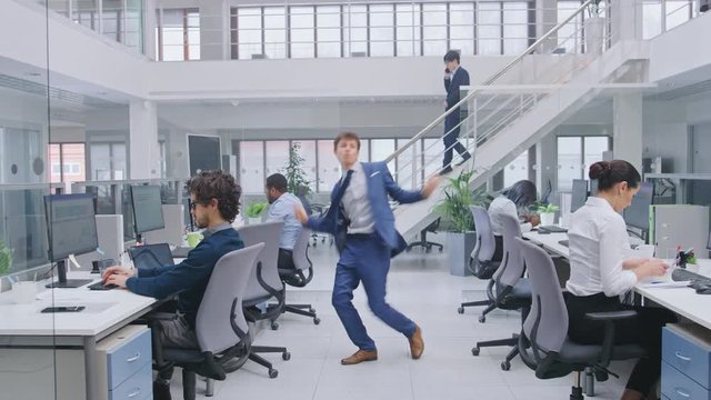 Young Cheerful Handsome Business Manager Wearing a Suit and Tie Dancing in the Office. Diverse and Motivated Business People Work on Computers in Modern Open Office.