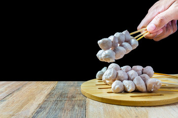 Fototapeta na wymiar Pork ball Thai style skewers is a very famous street food. Serve hot on a wooden tray with a black backdrop.