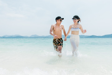 Full body portrait of  young women and men laughing and running on the beach