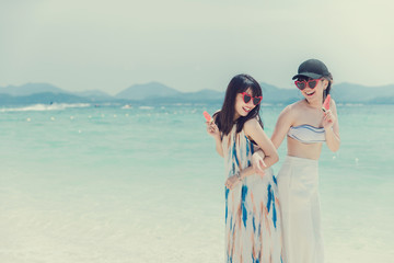 Full body portrait of two young women friends laughing and enjoy on the beach,In the hands holding a fruit.