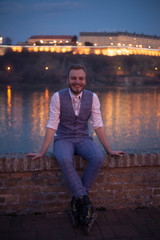 one young businessman sitting near a river while wearing inline blades.