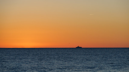 Naklejka na ściany i meble Orange sunset over the sea. The sun hides behind the horizon in the sea.