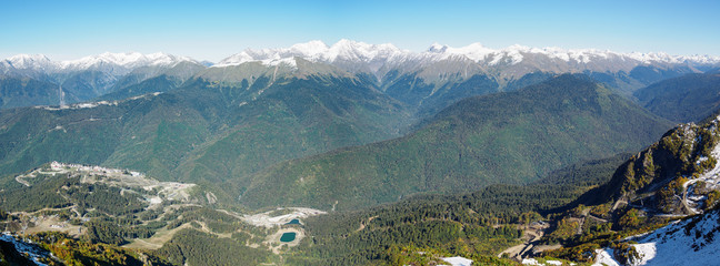 Panoramic view from the top of the Aibga mountain range to the ski resort Rosa Khutor. The valley is surrounded by high mountains with snowy slopes.