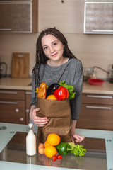 Woman holding full paper bag with products in hands on the background of the kitchen. Healthy and fresh organic food