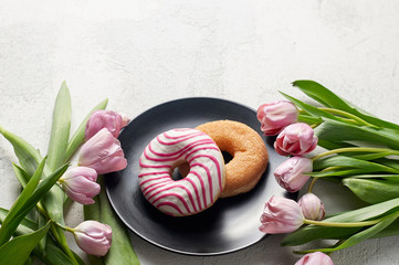 Obraz na płótnie Canvas Sugar and Striped-glazed donuts with tulips on black plate