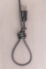 concept of energy dependence: a blurred hinge loop made of an electric cord with a plug, on a wooden background, toning, haze