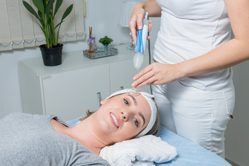 High frequency machine in spa salon. Young blond woman receiving electric darsonval facial massage...