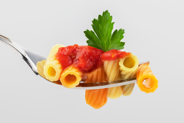 pasta on a fork with tomato sauce and parsley leaf close-up on a light gray background