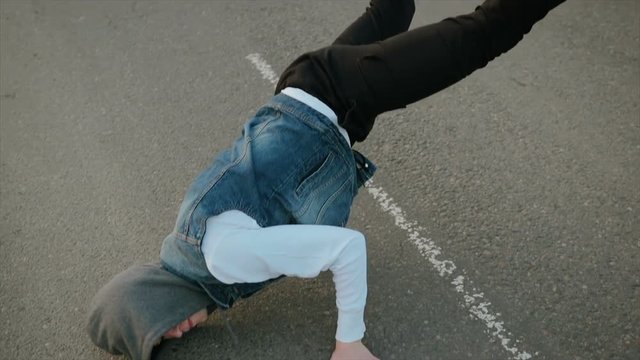 Slow motion of a modern young Caucasian guy dancing a lower break on an asphalt road with white markings, performing a handstand with his legs raised high. The concept of youth culture