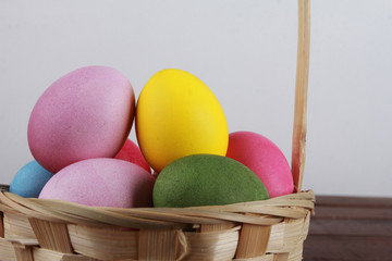 Painted eggs in basket on brown wooden table. Easter background concept. Pink, yellow, green, orange eggs, side view