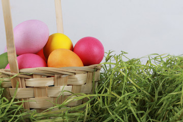 Painted eggs in basket with dry green grass. Easter background or egg hunt concept. Pink, yellow, green, orange eggs, hay, side view, close-up
