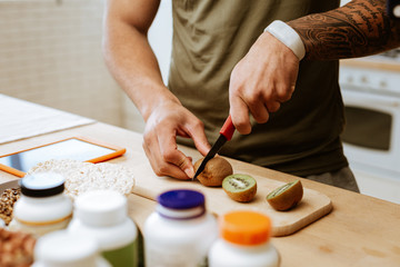 Obraz na płótnie Canvas Man with tattoo on hand holding knife while cutting kiwi
