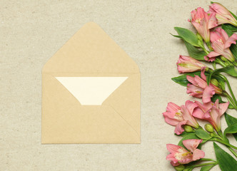 Beige craft envelope with white blank paper and flowers on stone background
