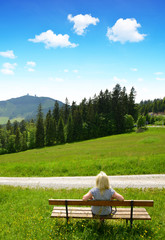 Tourist sitting on a bench overlooking the mount Grosser Arber in National park Bayerische Wald,...