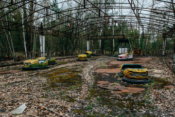 Old broken rusty metal radioactive yellow cars, children's electric cars, abandoned among...