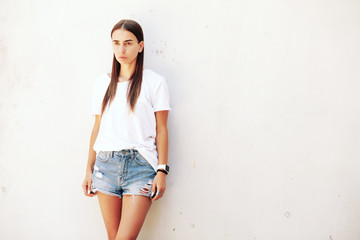  Fitness young girl with long legs in denim shorts and sneakers posing against the white wall