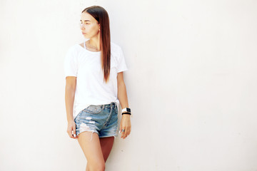  Fitness young girl with long legs in denim shorts and sneakers posing against the white wall
