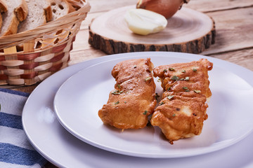 Deep-fried battered cod fillets, in a white plate next to onions and bread on a wooden background