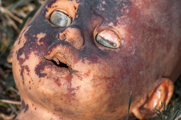 Fototapeta premium Creepy old doll head. Broken abandoned damaged scary toy in a garbage dump close-up. In the toy, the eye and mouth are damaged. The concept of fear, horror, crime. Very scary.