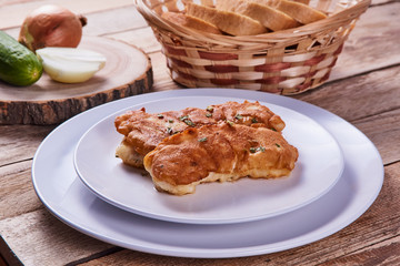 Deep-fried battered cod fillets, in a white plate next to onions, cucumber and bread on a wooden background. Close-up