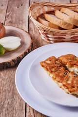 Deep-fried battered cod fillets, in a white plate next to onions, cucumber and bread on a wooden background. Close-up