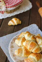 Freshly baked croissants on wooden cutting board on dark wooden table.