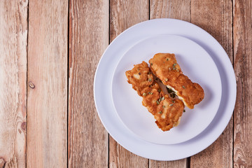 Deep-fried battered cod fillets, in a white plate on a wooden background. Flat lay