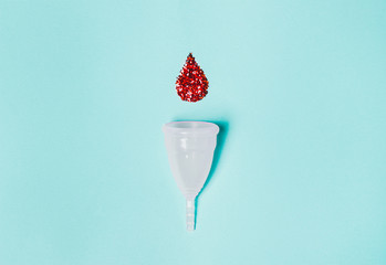 white menstrual cup  with a drop of blood on a blue background