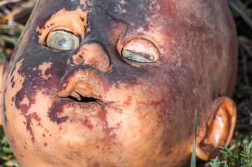 Obraz premium Creepy old doll head. Broken abandoned damaged scary toy in a garbage dump close-up. In the toy, the eye and mouth are damaged. The concept of fear, horror, crime. Very scary.