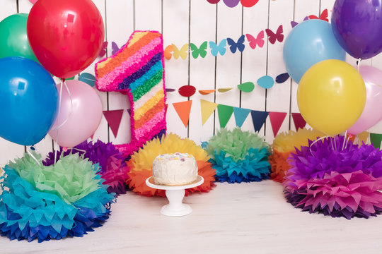 Photo zone with paper garlands, balloons, paper balls, pom poms, confetti and cream cake. Birthday cake. Smash cake. One year. Pink, white, blue, green, red,yellow colors