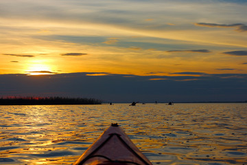 Bow of kayak and silhouettes of kayakers rowing on the lake at sunset